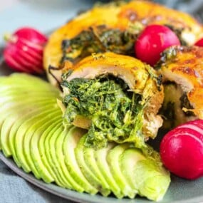 Rolled chicken stuffed with spinach beside avocado slices.