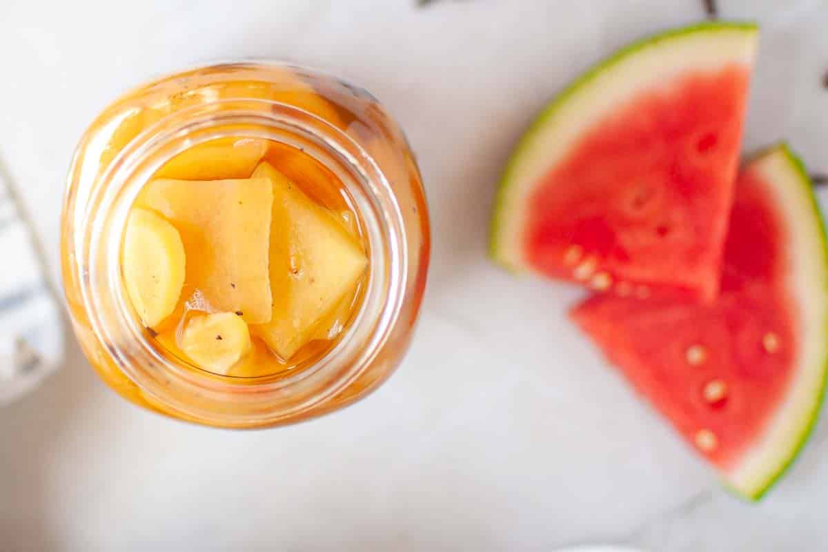 Pickled watermelon rind jar beside watermelon slices.