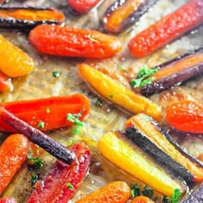 Roasted rainbow carrots with a light glaze and chopped herbs on a baking sheet.