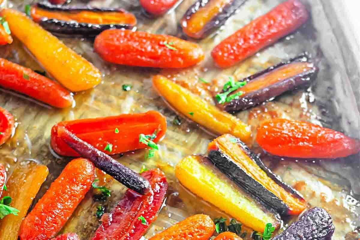 Roasted rainbow carrots with a light glaze and chopped herbs on a baking sheet.