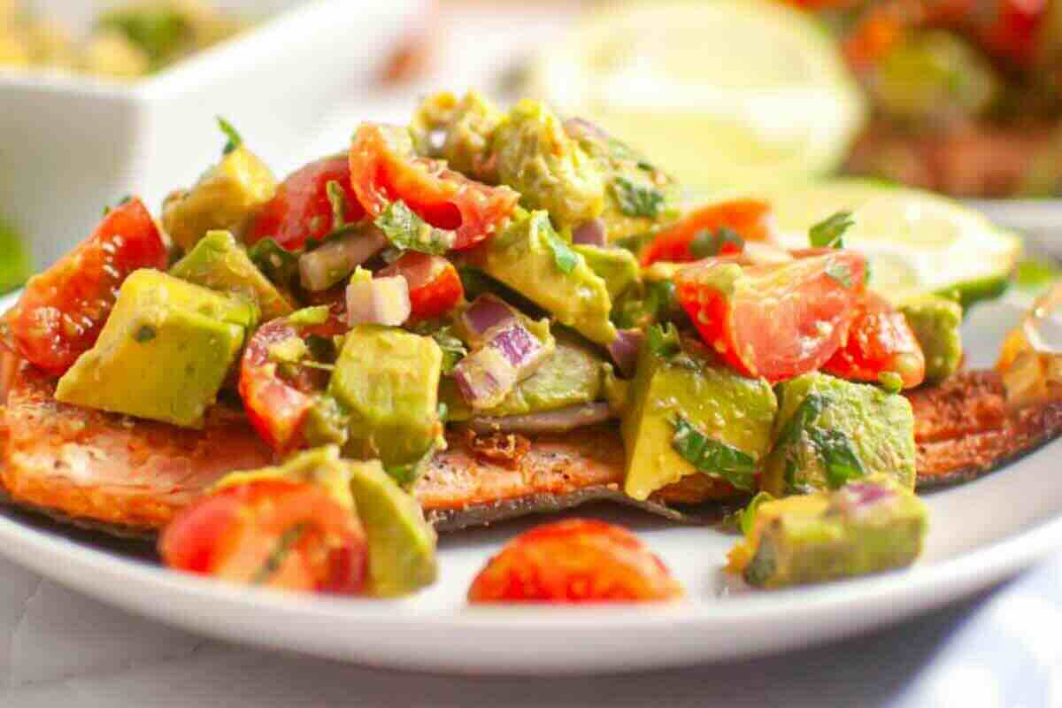 Grilled salmon fillet topped with a chunky avocado, tomato, and red onion salsa on a white plate.