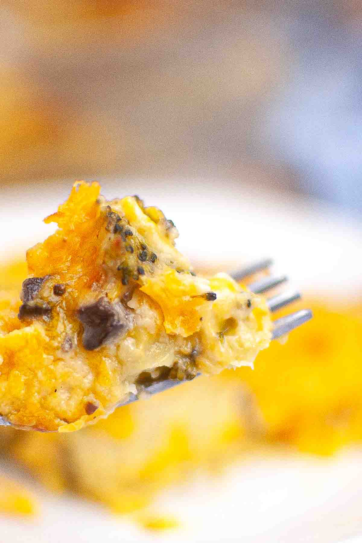 A close-up of a fork holding a cheesy broccoli and mushroom casserole, with melted cheese visible on top.