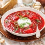 A bowl of red borscht topped with a dollop of sour cream and fresh dill.