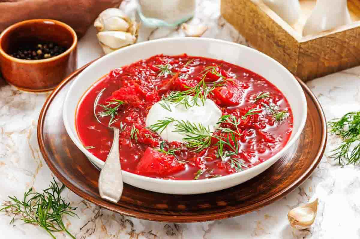 A bowl of bright red borscht topped with a dollop of sour cream and fresh dill, served with a spoon.
