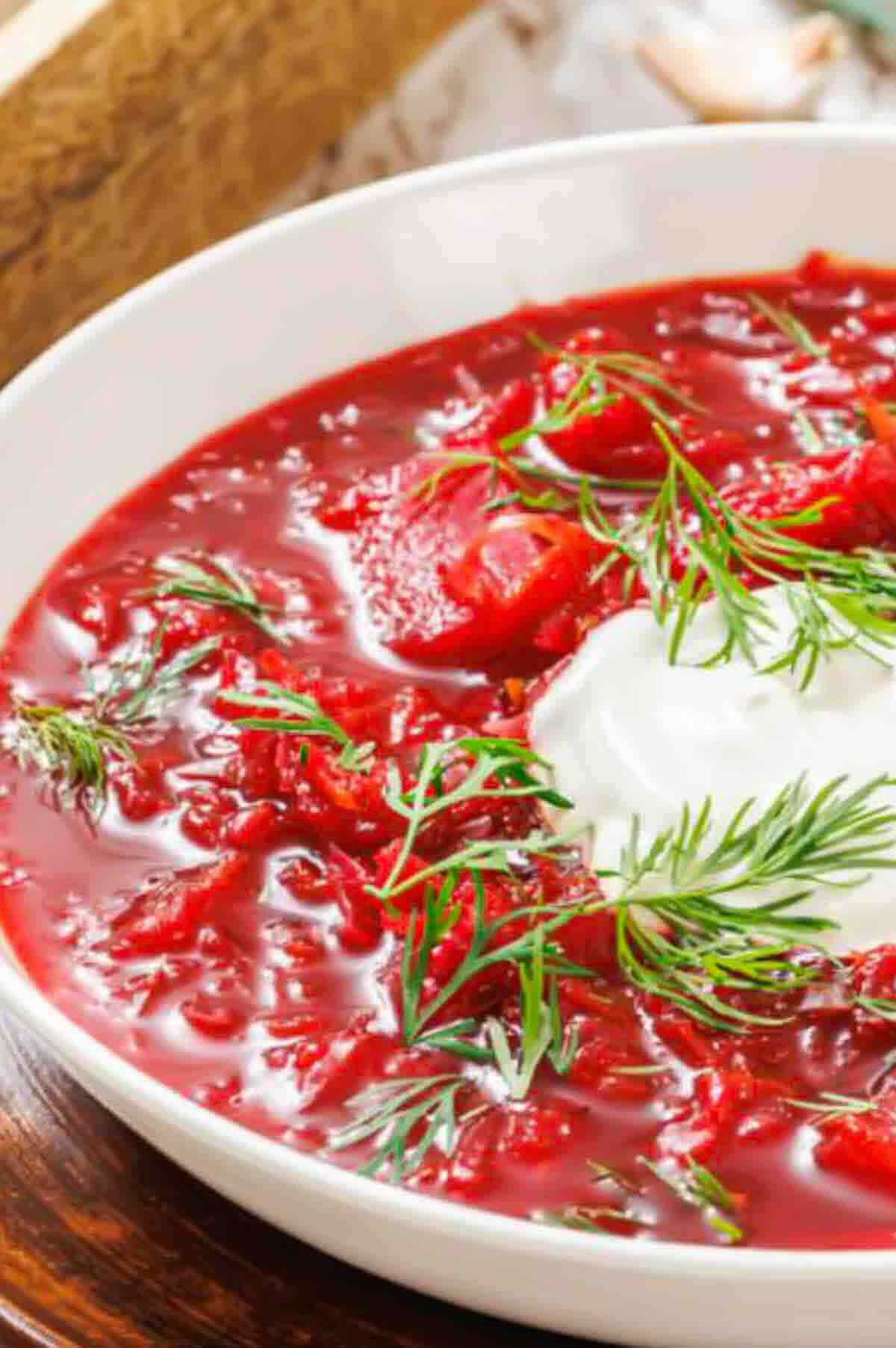 A bowl of red beet borscht topped with a dollop of sour cream and fresh dill.