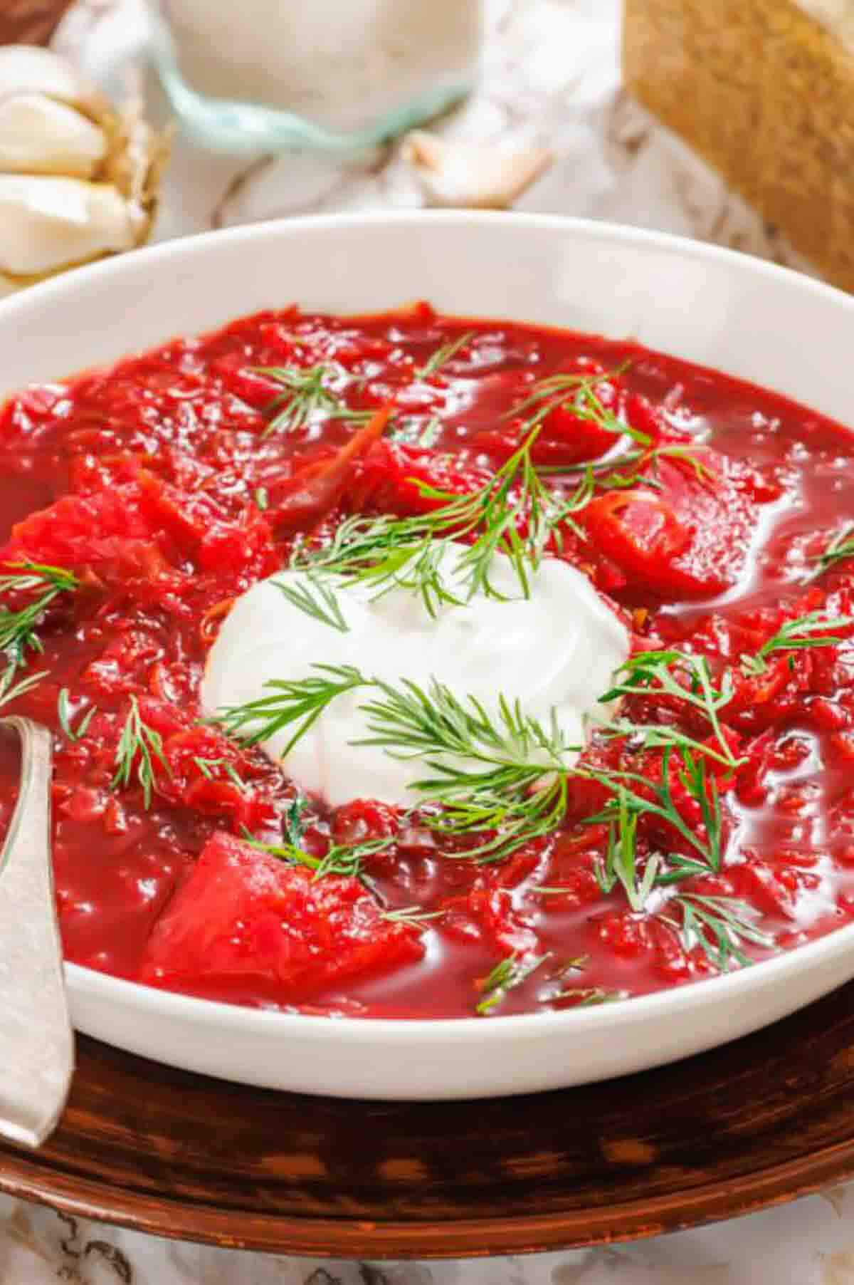 A bowl of red beet borscht topped with a dollop of sour cream and fresh dill.